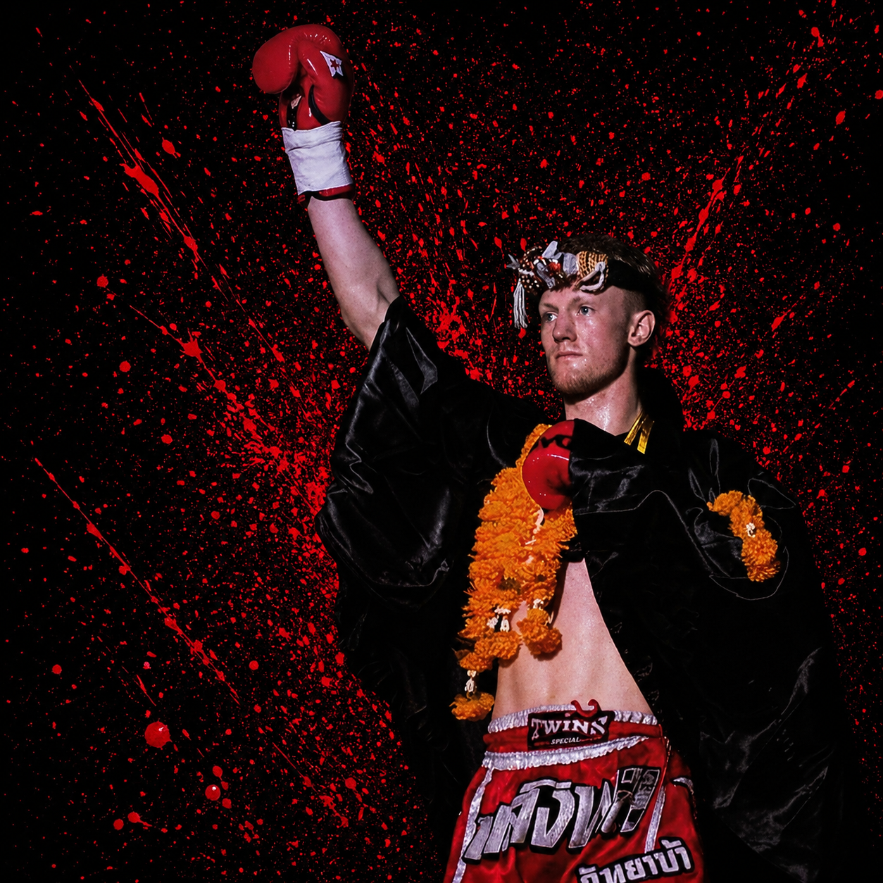 Alex MacGregor raising his glove in the ring wearing the traditional Mongkol and garland
